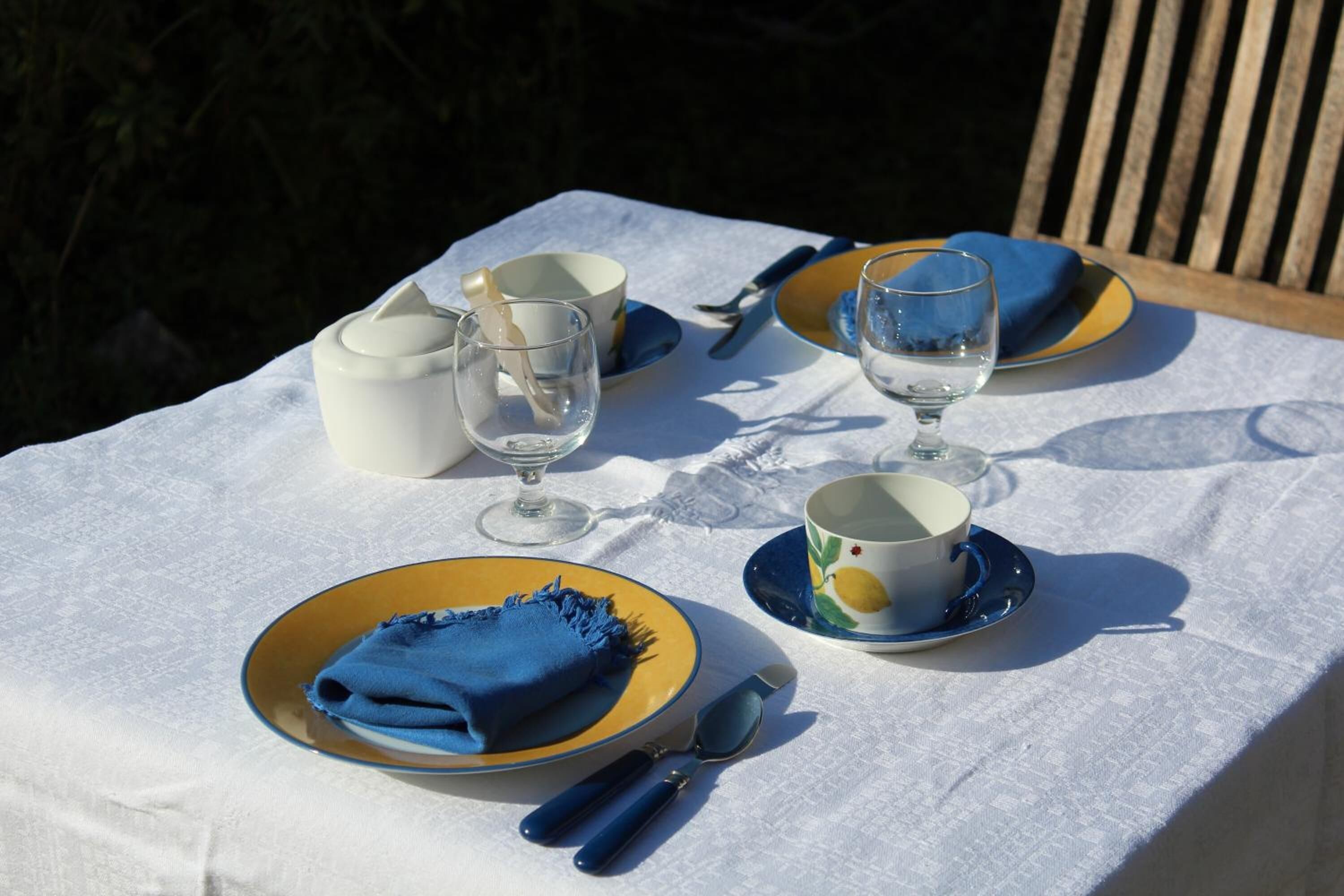 A table set outdoors with a white tablecloth, blue napkins, and yellow plates.