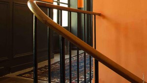 A staircase with a wooden handrail and black balusters, leading to a room with orange walls and a large window. - Chambres d'Hôtes de Parseval (Senlis)