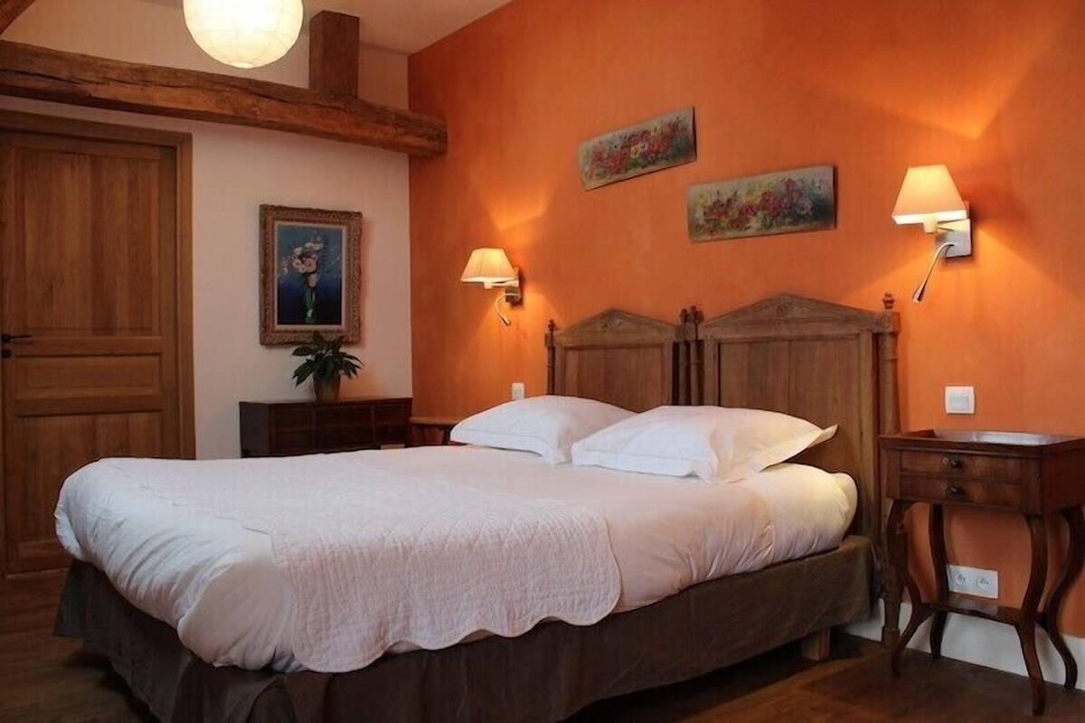 A bedroom with a large bed, wooden headboard, two wall-mounted lamps, a nightstand, and a wooden cabinet.