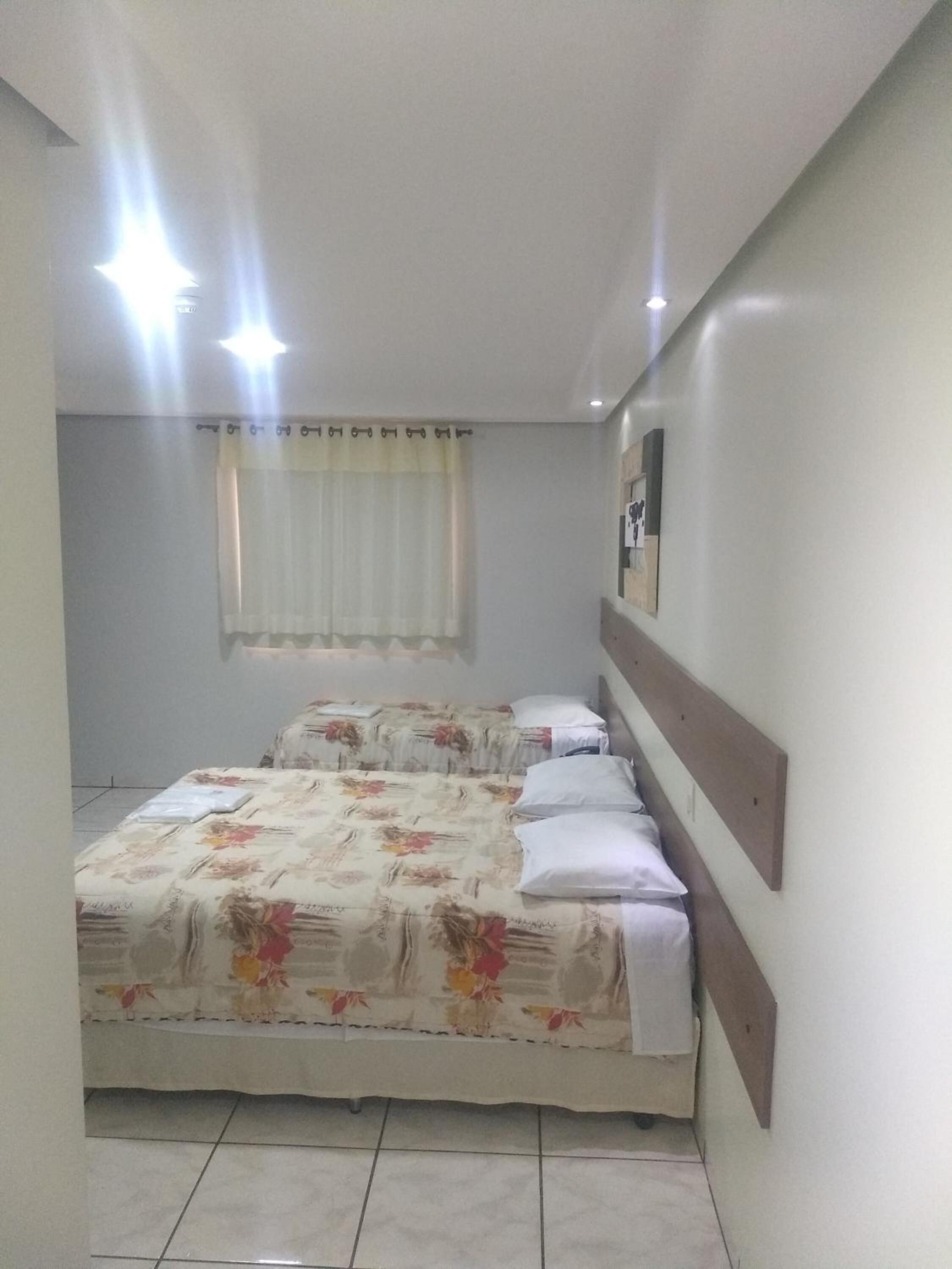 A small, clean room with two single beds, a window with curtains, and a wall-mounted mirror.