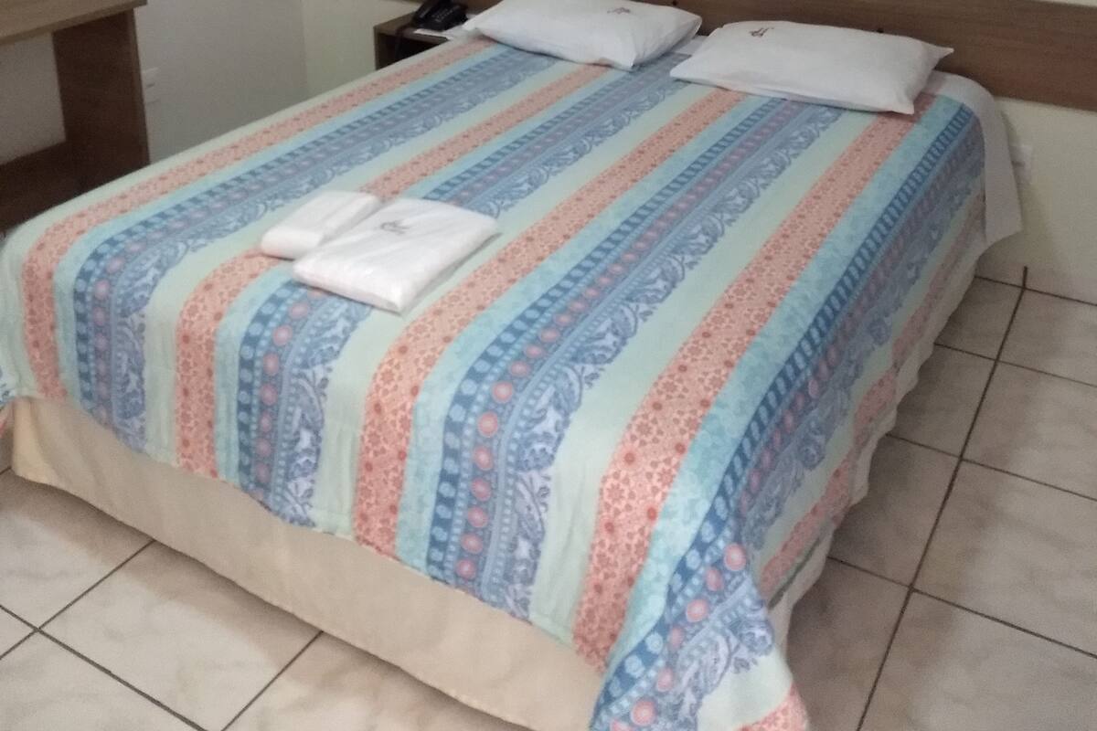 A bedroom with a bed, a bedside table, and a wall-mounted phone.