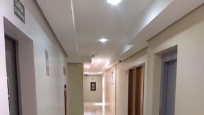 A long, well-lit hallway with tiled floors, doors on both sides, and a sign indicating the exit. - Hotel Soldera Inn (Sertaozinho)