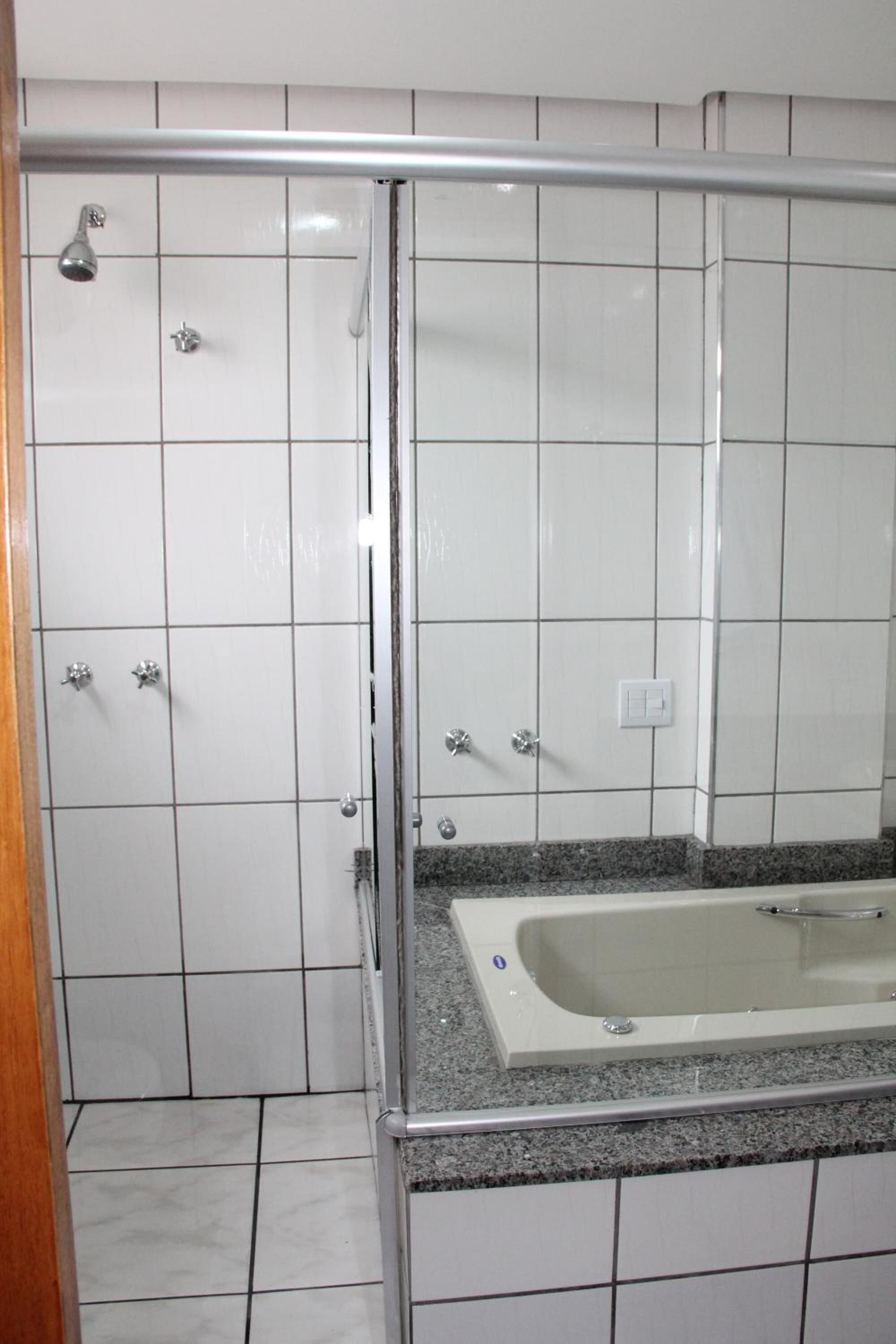 Une salle de bain avec des murs recouverts de carreaux blancs, une douche en verre, une baignoire et un comptoir en granit.