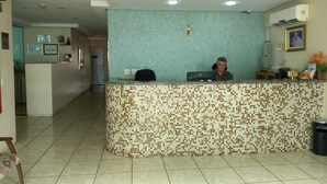 A reception area with a tiled mosaic counter, a cross on the wall, and a computer on the counter. - Hotel Soldera Inn (Sertaozinho)