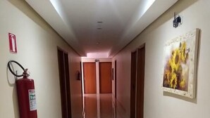 A hotel hallway with tiled floors, a fire extinguisher, and a painting on the wall. - Hotel Soldera Inn (Sertaozinho)