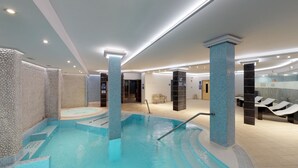 A modern indoor swimming pool with clear water, surrounded by stone-textured walls and columns, and equipped with a changing room and seating area. - HL Suites Nardos - Only Adults (San Bartolomé de Tirajana)