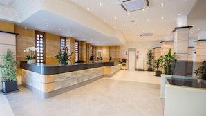 A hotel reception area with a curved reception desk, multiple potted plants, and a tiled floor. - HL Suites Nardos - Only Adults (San Bartolomé de Tirajana)