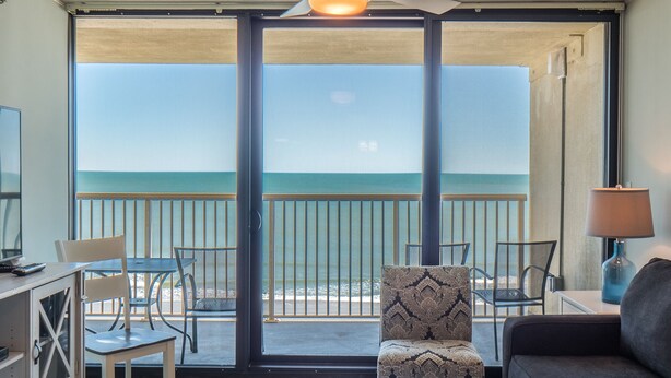 Habitación con balcón con vistas al mar, amueblada con sofá, sillas y una mesa.