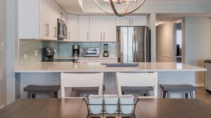 Una cocina moderna con armarios blancos, electrodomésticos de acero inoxidable, una isla grande con taburetes de bar y una lámpara central.