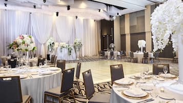 Een feestzaal met ronde tafels gedekt voor het diner, met witte tafelkleden en borden met gouden rand.
