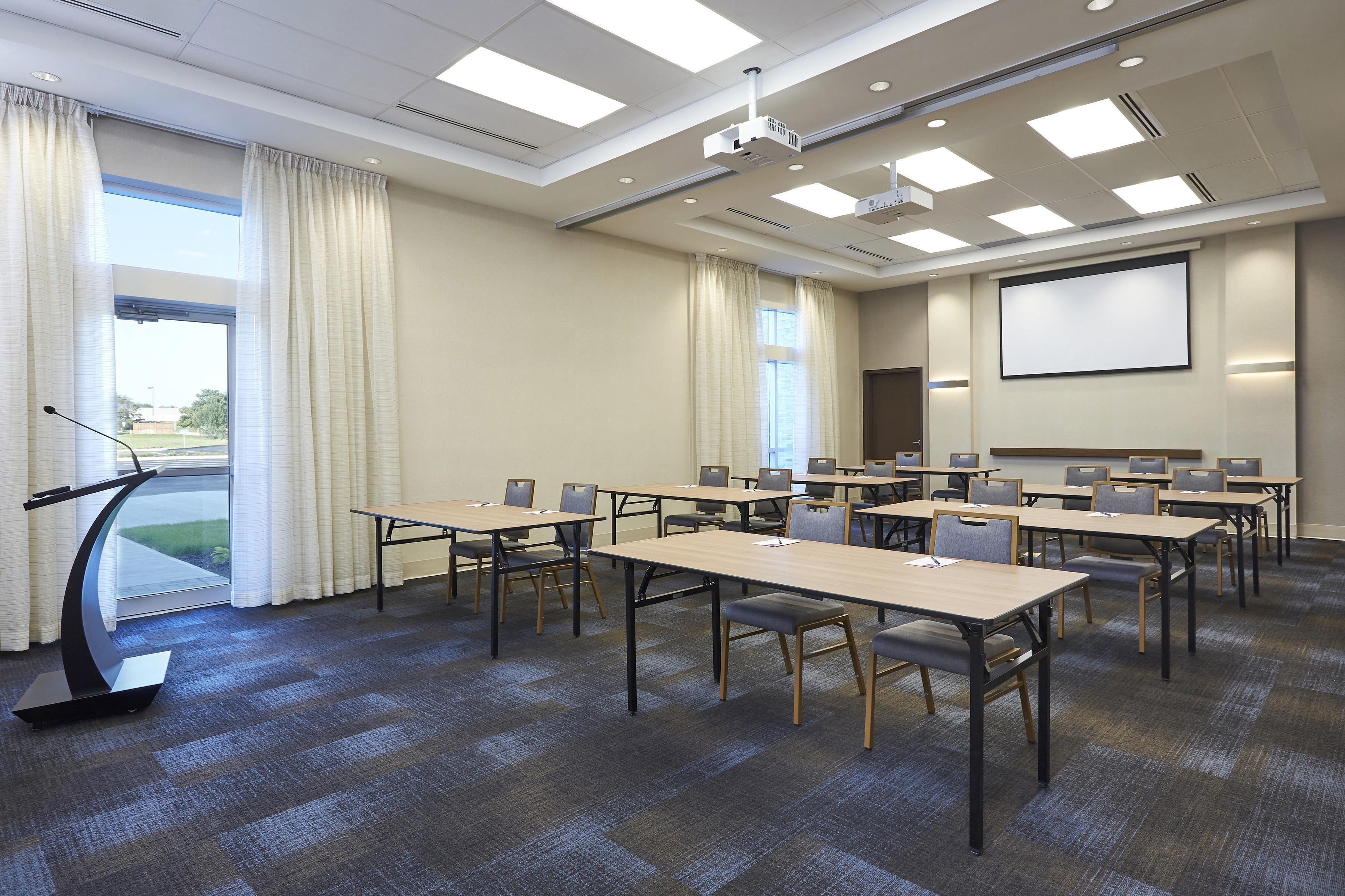 A conference room with tables, chairs, a projector, and a screen.