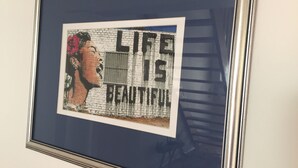 Ein gerahmtes Kunstwerk mit Schriftzug vor einer Backsteinwand.
