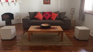 Ein Wohnzimmer mit grauem Sofa, roten Kissen, einem Holztisch und zwei weißen Hocker.