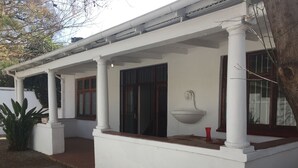 Ein weißes Gebäude mit einer überdachten Veranda, einem Steinweg und einem roten Blumentopf auf der Veranda.