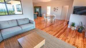 Ein modernes Wohnzimmer mit einer grauen Couch, einem Holztisch und einem Essbereich mit weißen Stühlen.