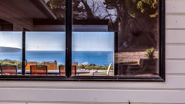 Ein Fenster mit Meerblick und eine Terrasse mit Stühlen und Tischen.