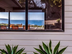Ein Fenster mit Meerblick und eine Terrasse mit Stühlen und Tischen.