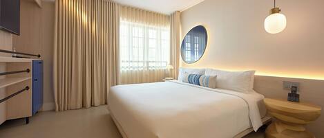 A hotel room with a large bed, a bedside table with a phone, a mirror, and a window with curtains.