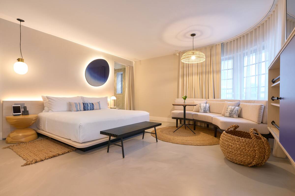 A modern hotel room with a large bed, a sofa, a small table, and a hanging light fixture.