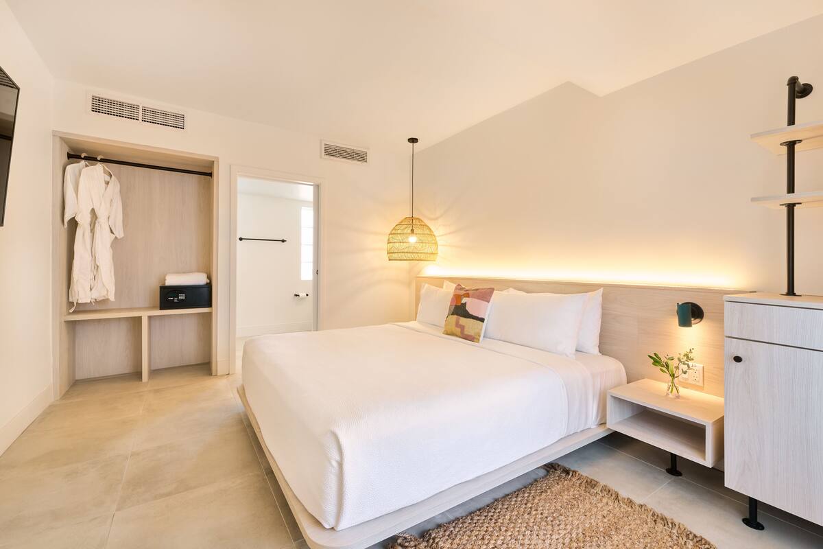 A modern bedroom with a large bed, bedside tables, a wardrobe, and a hanging light fixture.