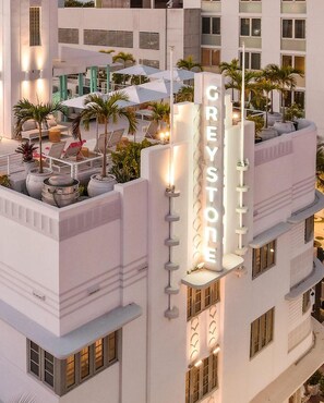 A hotel with a rooftop terrace featuring outdoor seating, palm trees, and a prominent 'GREYSTONE' sign.