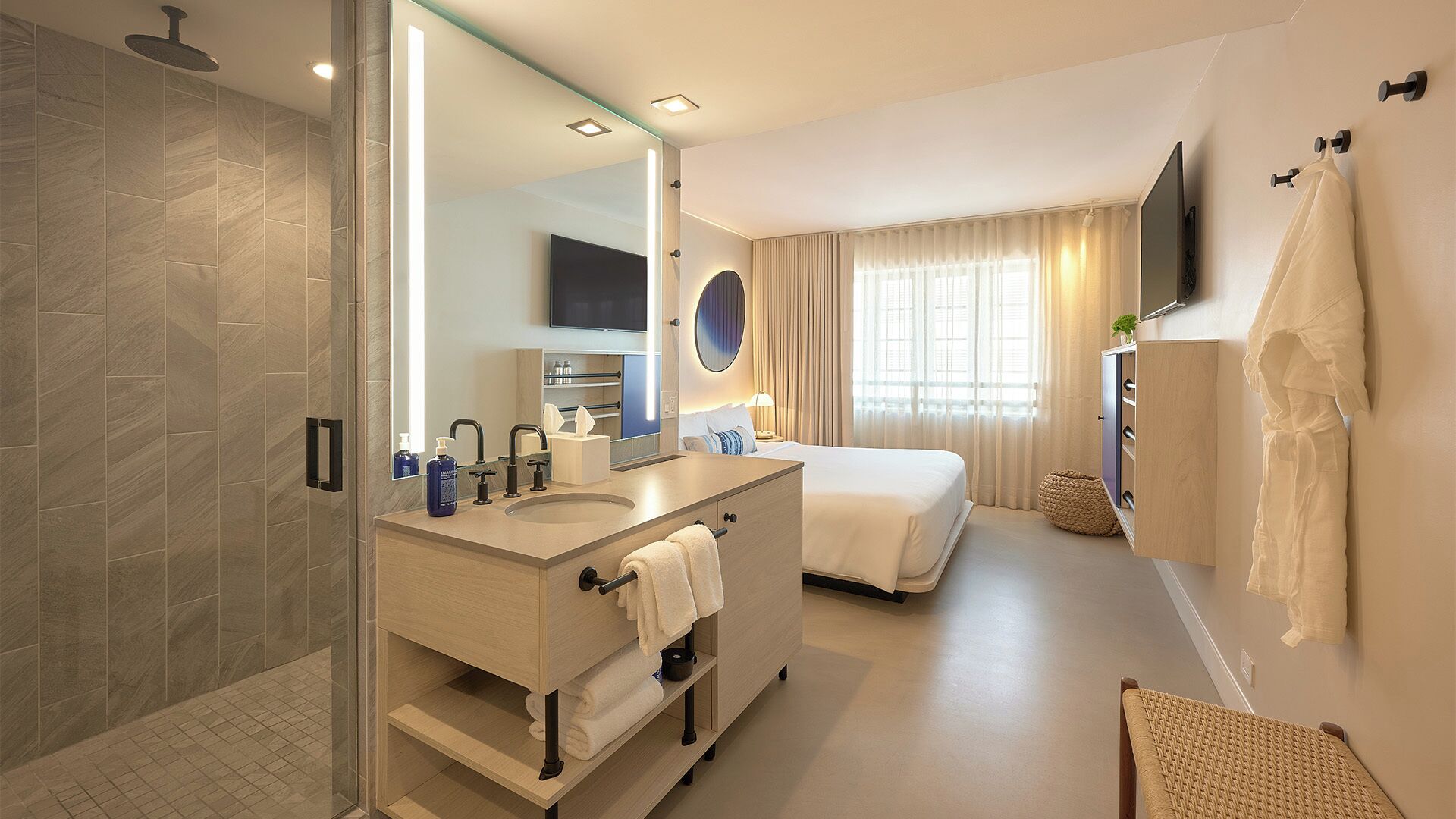 Une salle de bain d’hôtel avec une douche, deux lavabos, un grand miroir et un lit.