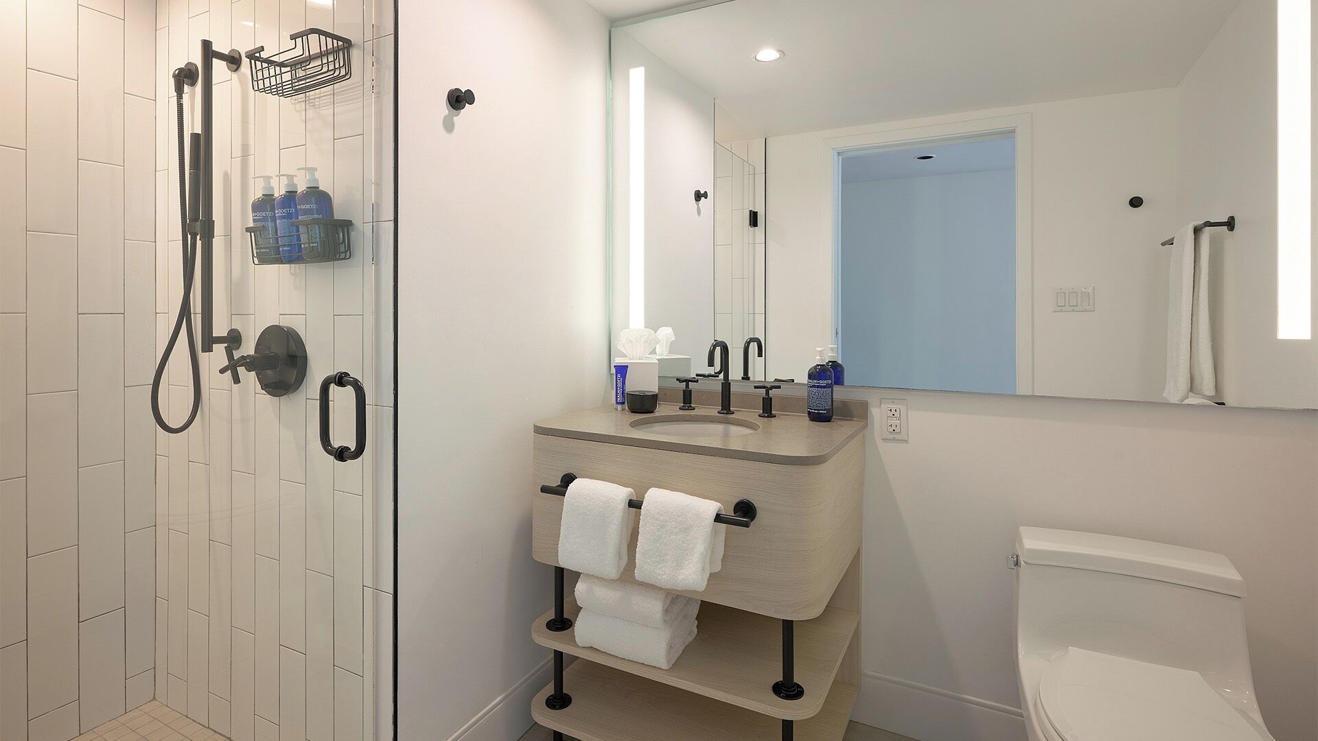 A modern bathroom with a shower, toilet, sink, and towel rack.