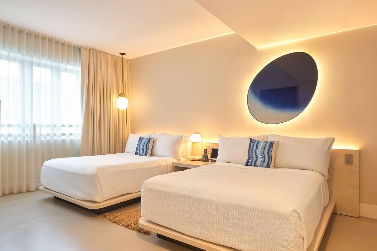 A hotel room with two beds, a large mirror, and a nightstand with a lamp.