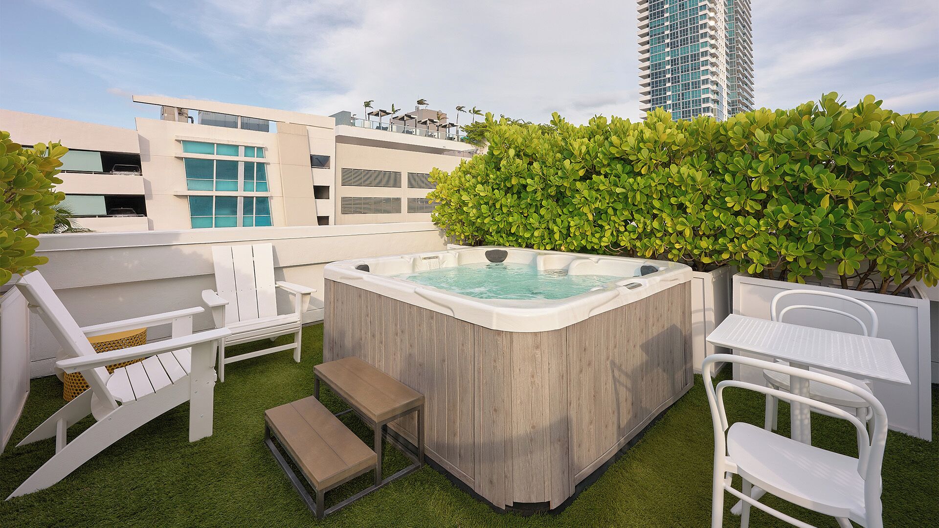 A rooftop terrace with a hot tub, seating area, and a view of modern buildings.