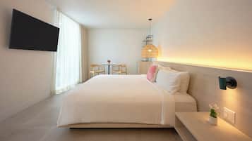 A modern hotel room with a large bed, a flat-screen TV mounted on the wall, a small table with chairs, and a wall-mounted lamp.