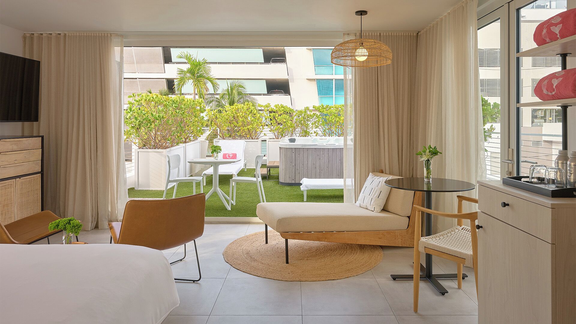 Quarto de hotel com cama, sofá, mesa de jantar, cadeiras, área de jardim com plantas, banheira de hidromassagem e vista para edifícios.