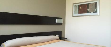 Habitación de hotel con una cama, una mesita de noche, un respiradero en la pared y un cuadro enmarcado.