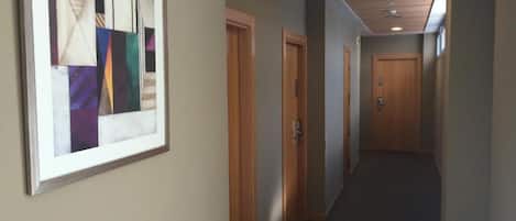 Un pasillo con puertas de madera, una obra de arte abstracto enmarcada en la pared e iluminación empotrada en el techo.