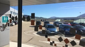 Un estacionamiento con varios coches y un edificio con un letrero con la letra 'H' al fondo.