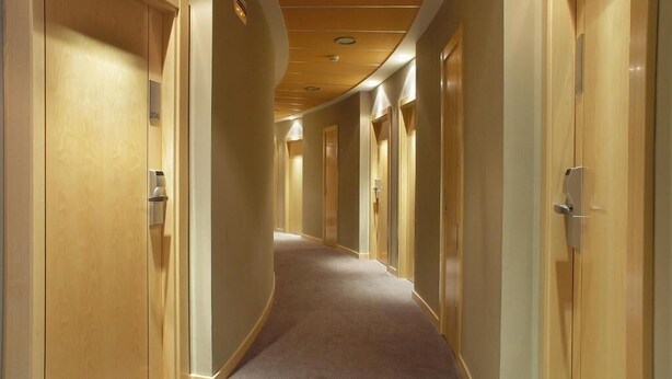 Un pasillo de hotel con puertas de madera, piso alfombrado y techo curvo con iluminación empotrada.