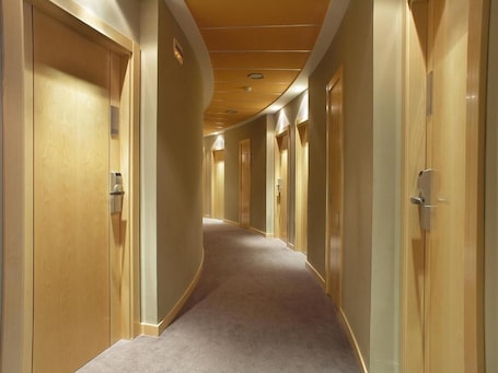 A hotel corridor with wooden doors, a carpeted floor, and a curved ceiling with recessed lighting.