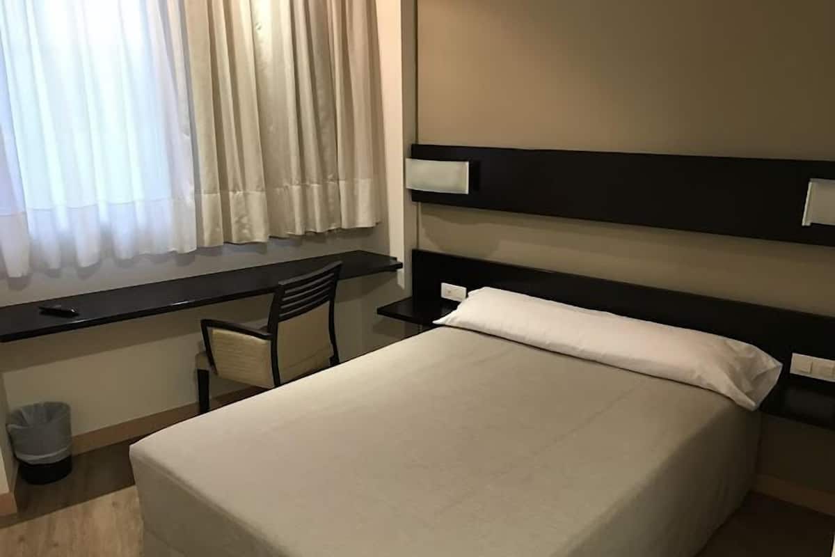 A hotel room with a bed, a desk, and a chair.