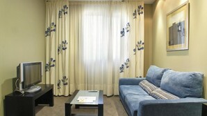 Una sala de estar con un sofá, una mesa de centro, un televisor sobre un mueble bajo y cortinas con estampado floral.
