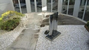 Un edificio moderno con fachada de vidrio curvada, un sendero de concreto y una escultura central.