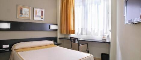 Habitación de hotel con cama, escritorio, silla, televisor y ventana con cortinas.