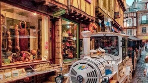 Une ruelle étroite pavée de pierres, où un tramway d’époque est garé devant une boutique nommée « ANTIQUE ».
