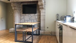 Une cuisine moderne avec un mur d’accent en pierre, un téléviseur à écran plat, une table en bois et un plan de travail sur lequel se trouve une machine à café.