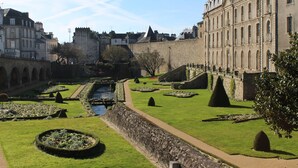 Une cour historique dotée d’une fontaine centrale, entourée de jardins magnifiquement entretenus et de murs en pierre.