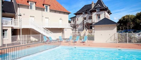 Una piscina con sillas de descanso, un edificio con tejado rojo y una escalera que conduce a un balcón.