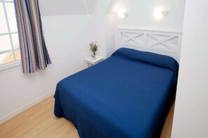 A bedroom with a bed, a nightstand, a potted plant, and a window with curtains.