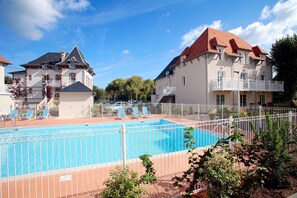 A swimming pool with lounge chairs, surrounded by a white fence, and adjacent to a building with a red roof.
