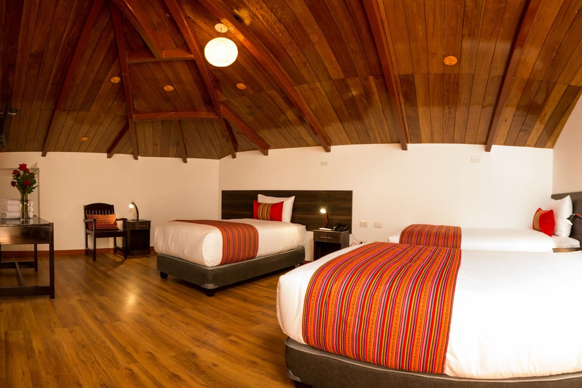 Une chambre spacieuse avec deux lits, un plancher en bois et un plafond haut avec des poutres apparentes.