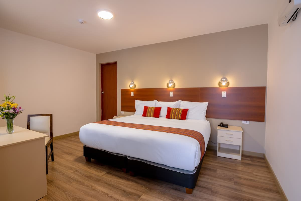 Une chambre d’hôtel avec un grand lit, des tables de chevet, un bureau et un vase de fleurs.