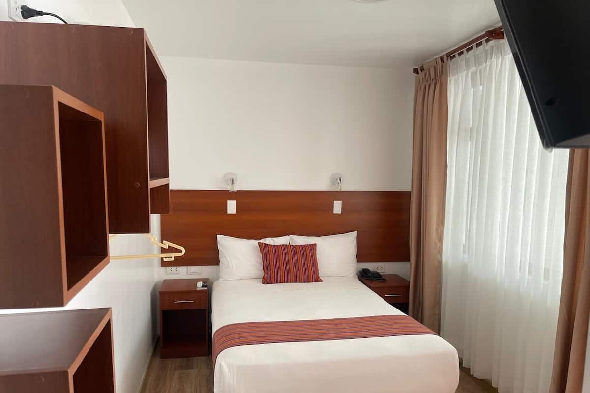 Une chambre d’hôtel avec un grand lit, une tête de lit en bois, des tables de chevet, une télévision et une fenêtre avec des rideaux.
