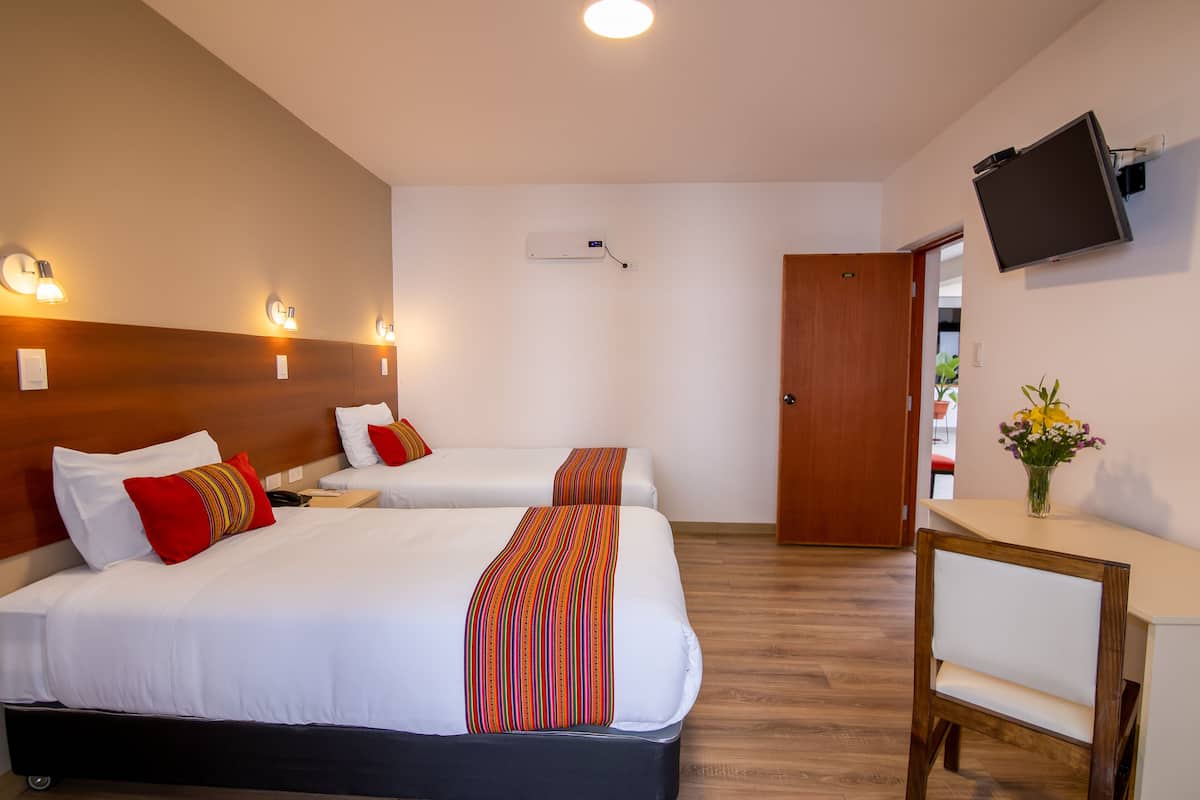 Une chambre d’hôtel avec deux lits, un bureau, une chaise, une télévision et une porte donnant sur une autre pièce.